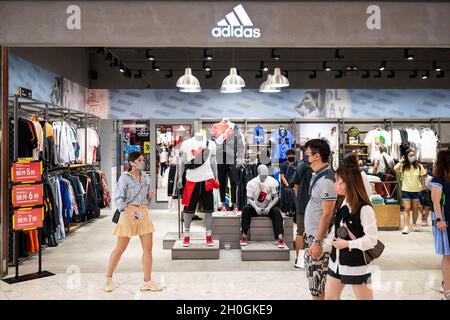 Die Käufer kommen an der deutschen multinationalen Sportartikelmarke Adidas-Store und -Logo in Hongkong vorbei. Stockfoto