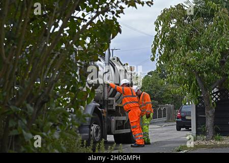 Straßenwartung. Diese Männer räumen einen Abfluss an der Bordsteinwand in einer Wohnstraße, um sicherzustellen, dass die Straße in Wickford, Essex, frei von Oberflächenwasser ist. Stockfoto