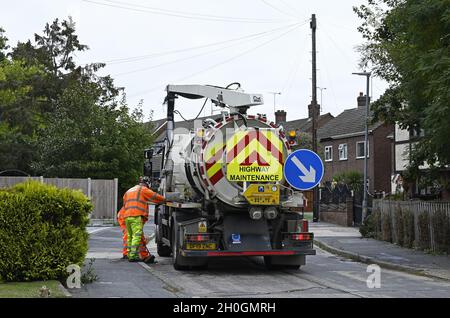 Straßenwartung. Diese Männer räumen einen Abfluss an der Bordsteinwand in einer Wohnstraße, um sicherzustellen, dass die Straße in Wickford, Essex, frei von Oberflächenwasser ist. Stockfoto