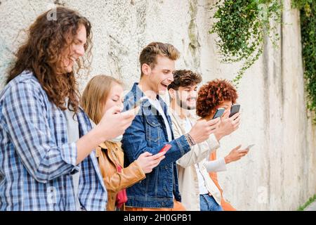 Multikulturelle Gruppe von Freunden, die Handys im Freien benutzen - Studenten surfen im Internet und halten Smartphones neben der Wand Stockfoto