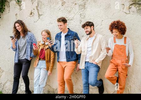 Multikulturelle Gruppe von Freunden, die Handys im Freien benutzen - Studenten surfen im Internet und halten Smartphones neben der Wand Stockfoto