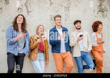 Multikulturelle Gruppe von Freunden, die Handys im Freien benutzen - Studenten surfen im Internet und halten Smartphones neben der Wand Stockfoto