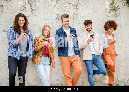 Multikulturelle Gruppe von Freunden, die Handys im Freien benutzen - Studenten surfen im Internet und halten Smartphones neben der Wand Stockfoto