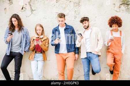 Multikulturelle Gruppe von Freunden, die Handys im Freien benutzen - Studenten surfen im Internet und halten Smartphones neben der Wand Stockfoto