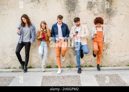 Multikulturelle Gruppe von Freunden, die Handys im Freien benutzen - Studenten surfen im Internet und halten Smartphones neben der Wand Stockfoto