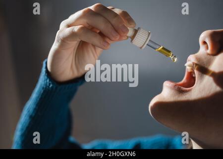 Sublinguales cbd-Hanföl - Frau, die Cannabidiol zur alternativen Angstbehandlung unter die Zunge nimmt - Fokus auf die Hand, die Tropf hält Stockfoto