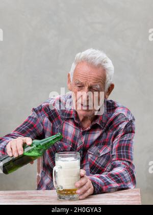 Älterer betrunkener Mann, der am Tisch sitzt und Bier trinkt Stockfoto