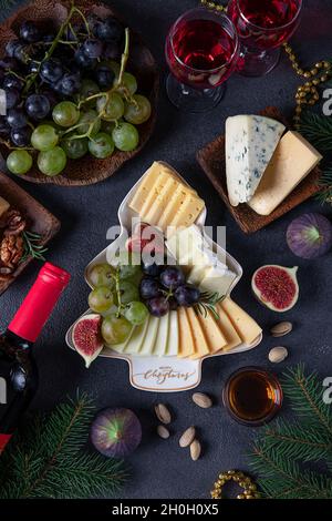 Verschiedene Käsesorten und Früchte, serviert auf einem Teller als Weihnachtsbaum, auf dunkelgrauem Hintergrund mit zwei Gläsern Wein. Silvesterparty-Snack Stockfoto