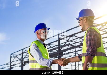 Zwei Ingenieure schüttelten Hand auf der Baustelle mit Metallkonstruktion im Hintergrund Stockfoto