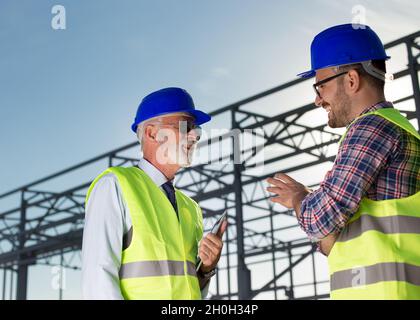 Leitender Ingenieur und Bauarbeiter im Gespräch vor der Metallkonstruktion auf der Baustelle Stockfoto