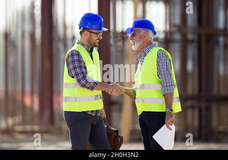 Zwei Ingenieure schüttelten Hand auf der Baustelle mit Metallkonstruktion im Hintergrund Stockfoto