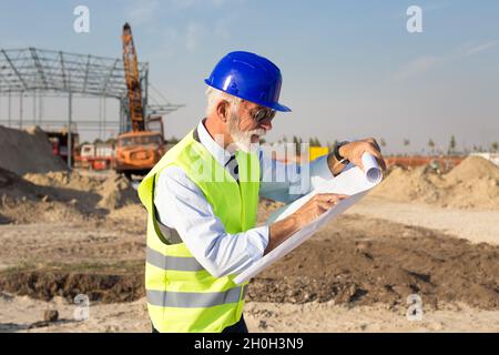 Leitender Ingenieur, der sich die Baupläne vor der Metallkonstruktion auf der Baustelle ansieht Stockfoto