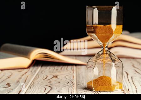Sandglas auf Holztisch mit geöffnetem Buch aus nächster Nähe Stockfoto