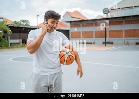 Ein Basketballspieler telefoniert, während er den Ball im Stehen hält Stockfoto