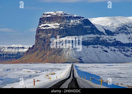 Gerade, schneebedeckte Straße in Richtung Berg, Winterlandschaft, Lomagnupur, Skeioararsandur, Südisland, Island Stockfoto