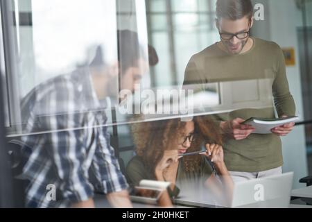 Drei junge, fokussierte Kollegen oder Kollegen, die Laptop betrachten und neue Projekte diskutieren, während sie im modernen Büro zusammenarbeiten Stockfoto