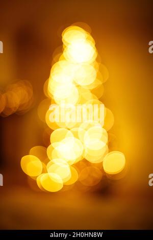 Leuchtend goldene Bokeh-Lichter in Christbaumform. Festlicher unscharfer Hintergrund. Stockfoto
