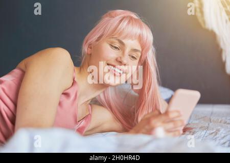 Junge Frau mit hellen Haaren schaut auf den Handybildschirm im Bett Stockfoto