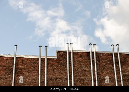 Rote Backsteinmauer mit Metallkaminen unter blauem Himmel an einem Tag Stockfoto