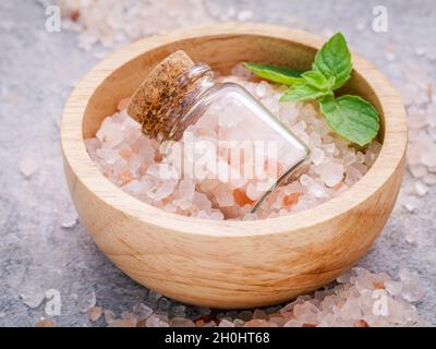 Closeup Himalaya Pink salt in Houten und Flasche mit Pfefferminze Blätter auf Stein. Himalaya-salz häufig in Kochen und für bat verwendet Stockfoto