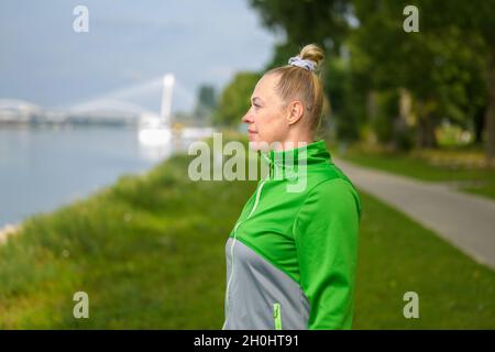 Fit gesunde Frau genießen ein Joggen entlang eines Flussufers Pause, um die Aussicht mit einem sile in einem Nahaufnahme Oberkörper Porträt in einem aktiven Lebensstil CO zu bewundern Stockfoto