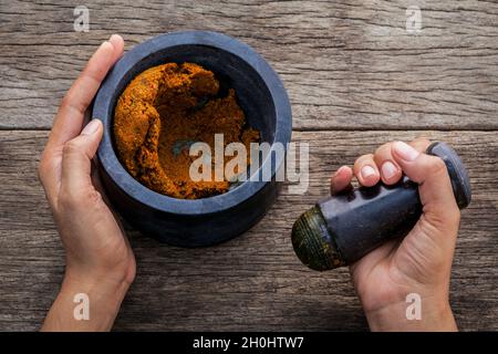 Die Frauen halten mit Mörser und Pistill Spice einfügen. Die rote paste Zutaten für Rot auf rustikalen Holzmöbeln Hintergrund Curry. Die Zutaten zum Kochen für p Stockfoto