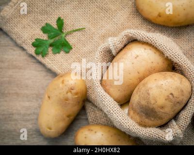 Closeup frische organische Kartoffeln in Hanf willen Tasche mit Petersilie auf rustikalen Holztisch Vorbereitung für das Kochen. Selektiver Fokus Tiefenschärfe. Stockfoto