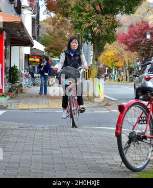 Karuizawa, Japan - 7. November 2019. Frau, die auf der Straße in Karuizawa, Japan, Radfahren kann. Karuizawa ist ein Resort in den Bergen von Nagano, berühmt für seine Herbst na Stockfoto