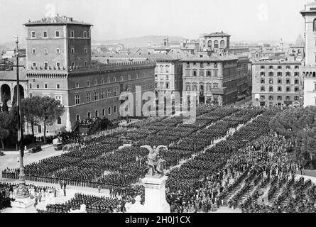 Vor einem Rednerstand, der 1935 vor dem Palazzo Venezia auf der Piazza Venezia in Rom stand, hat sich eine Parade versammelt (links). Die Regimenter besetzen den gesamten Platz vom Vittoriano bis zum Palazzo Bonaparte (im Hintergrund, Mitte des Bildes). Unten rechts sind Radsporttruppen und Motorradtruppen aufgestellt. [Automatisierte Übersetzung] Stockfoto