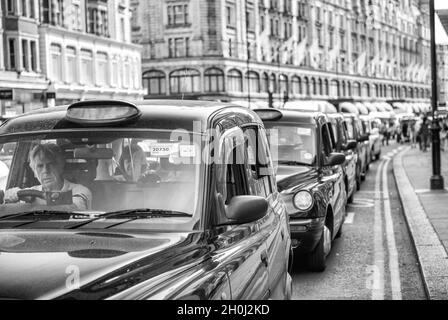 LONDON, Großbritannien - 3. JULI 2015: Stadtverkehr entlang einer verstopften Straße. Reihe schwarzer Taxis Stockfoto