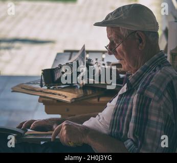 Älterer Mann, der im Garten sitzt und alte Fotos ansieht. Nostalgie- und Erinnerungskonzept Stockfoto
