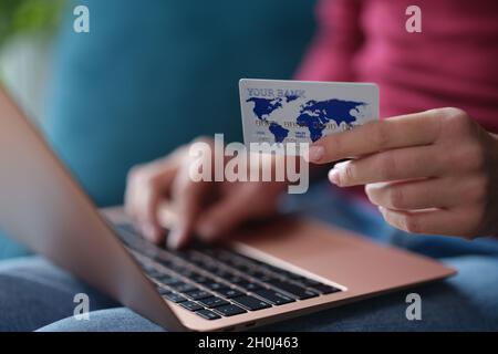 Frau hält die Bankkarte in den Händen und gibt Daten in die Nahaufnahme des Laptops ein Stockfoto