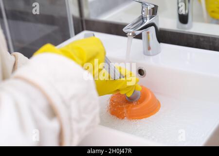 Eine Person mit gelben Handschuhen reinigt das Waschbecken von einer Blockierung aus der Nähe Stockfoto