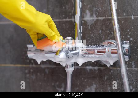 Hand in gelber Handschuh wäscht verchromten Mixer mit Waschlappen im Badezimmer Stockfoto