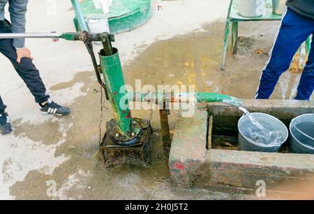 Pumpen von Wasser aus einer alten rostrosen, lackgeschälten Wasserpumpe in einen Zinnmetalleimer in Turkistan, Kasachstan Stockfoto