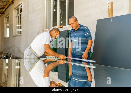 Ein Mann misst Spiegelglas mit einem Lineal, um es für die Verwendung in der lokalen Möbelproduktion zu schneiden Stockfoto