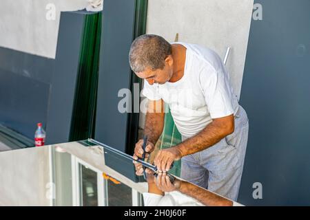 Ein Mann misst Spiegelglas mit einem Lineal, um es für die Verwendung in der lokalen Möbelproduktion zu schneiden Stockfoto