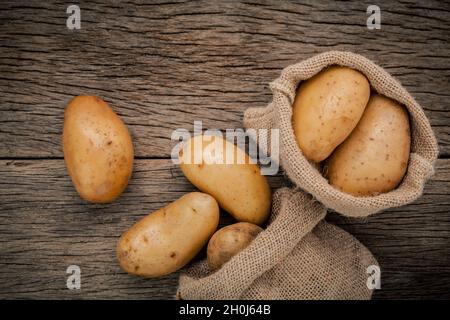 Frische organische Kartoffeln in Hanf willen Beutel auf rustikalen Holzmöbeln Hintergrund. Zeile bio Kartoffeln auf alten hölzernen Hintergrund mit kopieren. Stockfoto