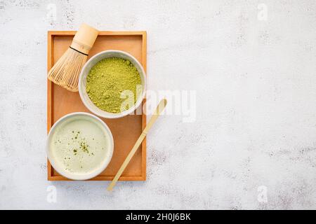 Matcha Grünteepulver mit Bambus Matcha Schneebesen Pinsel Setup auf weißem Beton Hintergrund. Stockfoto