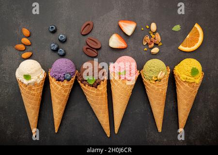 Verschiedene Eis Geschmack in Zapfen Heidelbeere, Pistazie, Mandel, Orange und Schokolade Setup auf dunklen Stein Hintergrund. Sommer und Süße Menükonzept Stockfoto