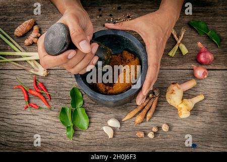 Die Frauen halten mit Mörser und Pistill spice Red Curry Paste Wirkstoff von Thai beliebte Speisen auf rustikalen Holzmöbeln Hintergrund. Gewürze Zutaten Chili, pe Stockfoto