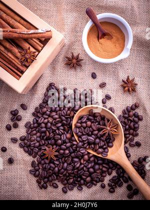 Die Löffel Kaffee Bohnen auf dem Tuch Sack mit Zimtstangen, Zimtpulver in der Schüssel und Sternanis. Stockfoto