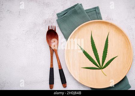 Essen konzeptuelles Bild eines Cannabisblattes mit Löffel und Gabel auf weißem Beton Hintergrund. Stockfoto