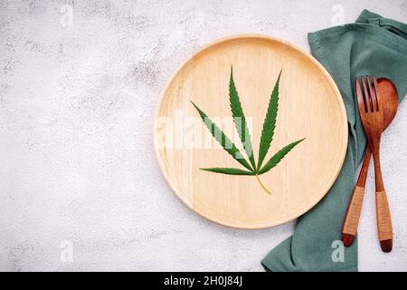 Essen konzeptuelles Bild eines Cannabisblattes mit Löffel und Gabel auf weißem Beton Hintergrund. Stockfoto