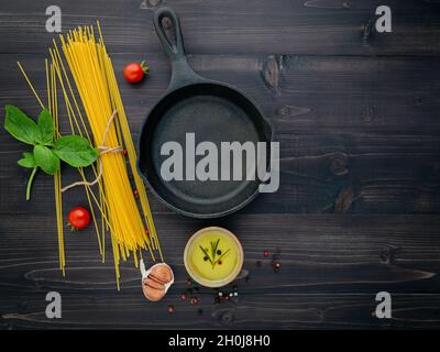 Die dünne Spaghetti auf schwarzem Holz- Hintergrund. Gelb italienische Pasta mit Zutaten. Italienisches Essen und Menü Konzept. Stockfoto