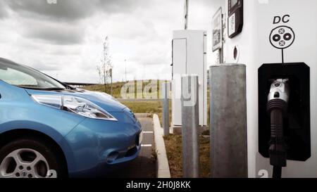 Nahaufnahme einer elektrischen Ladestation und eines blauen Elektroautos auf dem Parkplatz Stockfoto