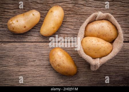 Frische organische Kartoffeln in Hanf willen Beutel auf rustikalen Holzmöbeln Hintergrund. Zeile bio Kartoffeln auf alten hölzernen Hintergrund mit kopieren. Stockfoto