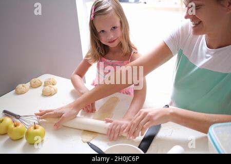 Lächelnde Mutter und Tochter Rollen den Teig mit Nudelholz aus der Nähe aus Stockfoto