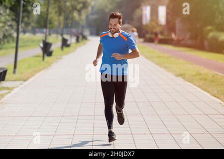 Zufriedener, gutaussehender Mann, der im Park läuft. Joggen am Morgen in der Stadt Stockfoto