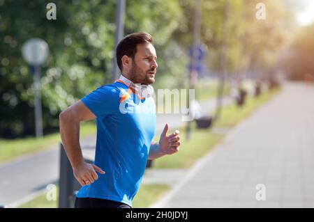 Zufriedener, gutaussehender Mann, der im Park läuft. Joggen am Morgen in der Stadt Stockfoto